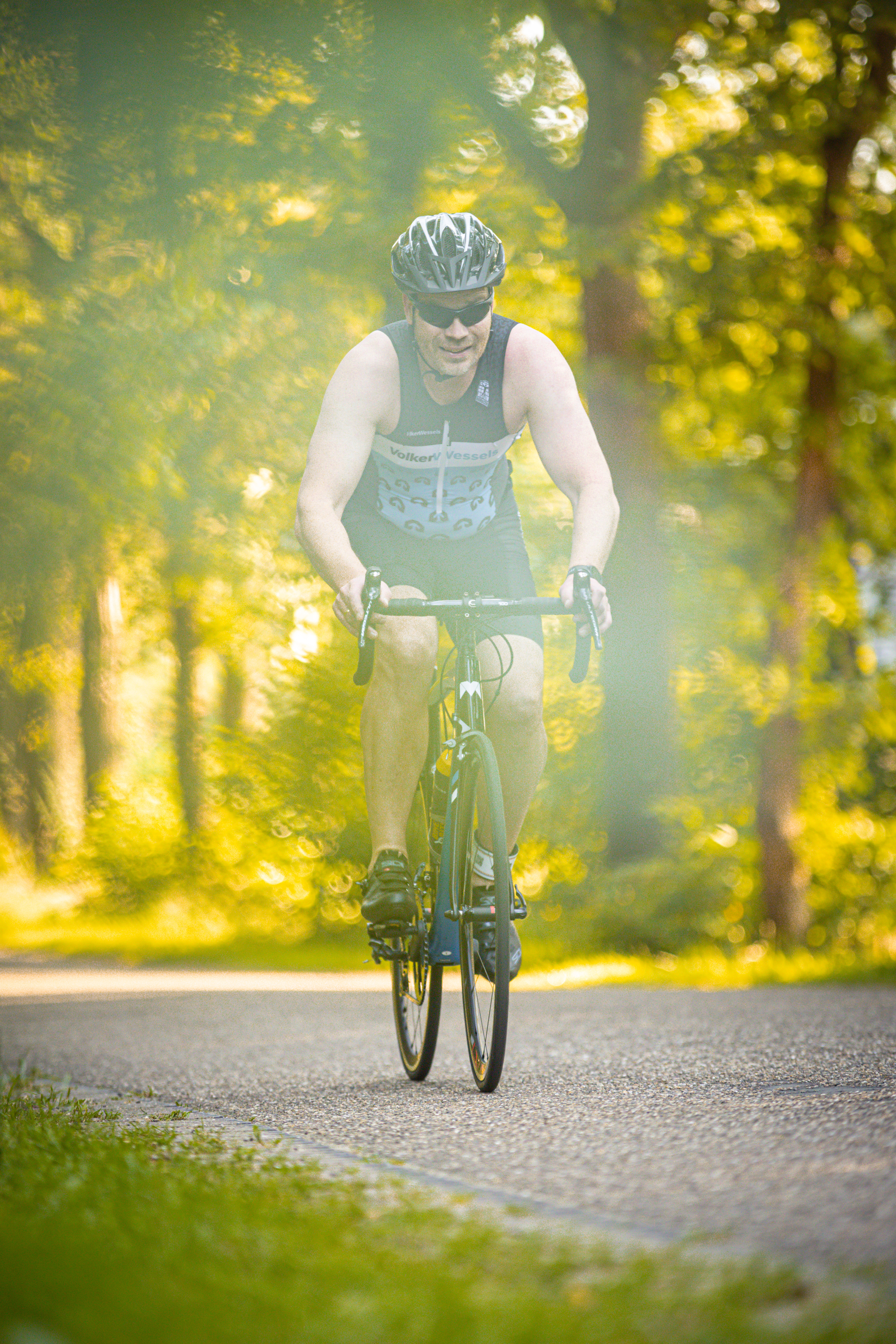 A man is riding a bicycle through the woods wearing a black tank top and bike helmet.