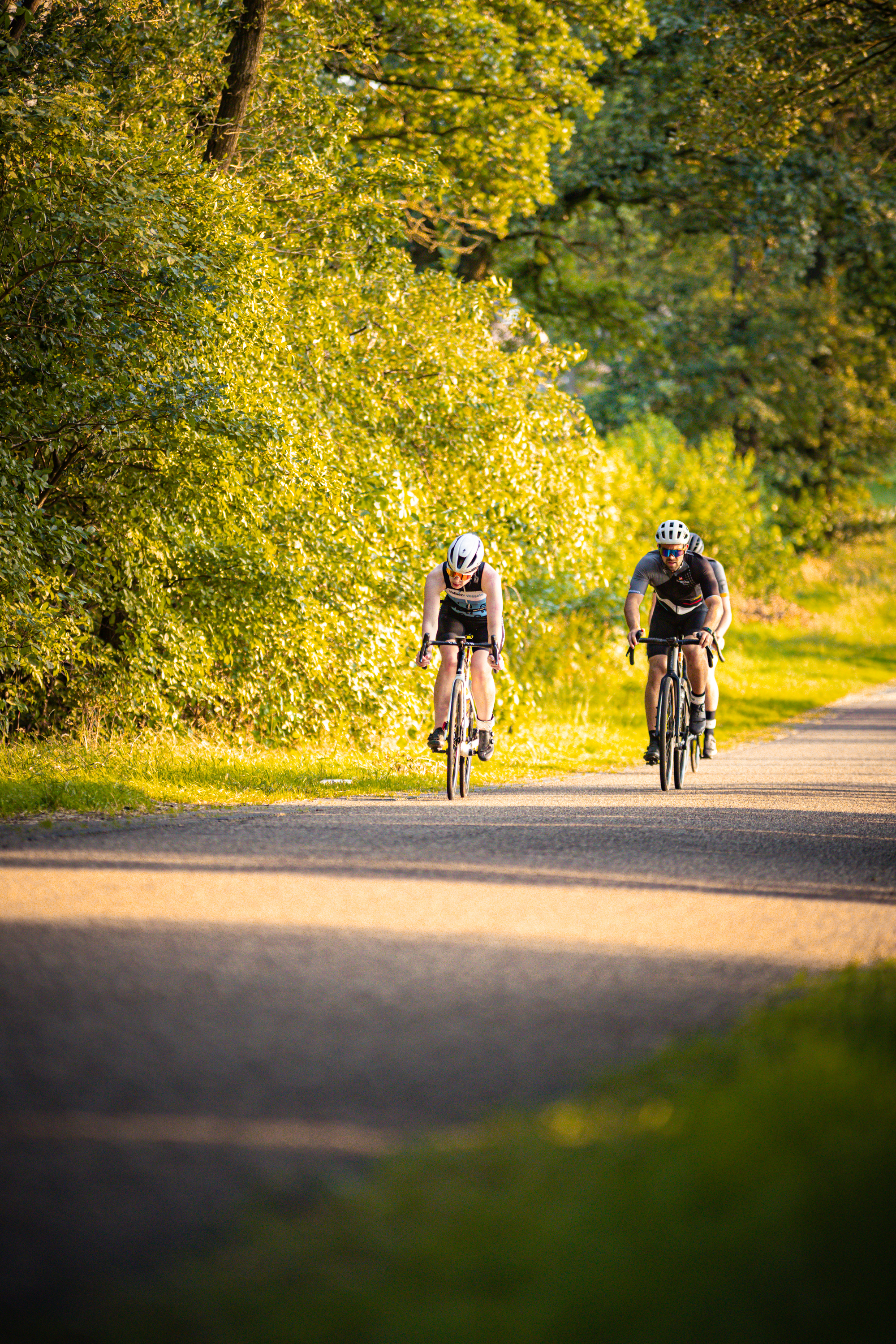 Two cyclists on a paved path, one with a white helmet.