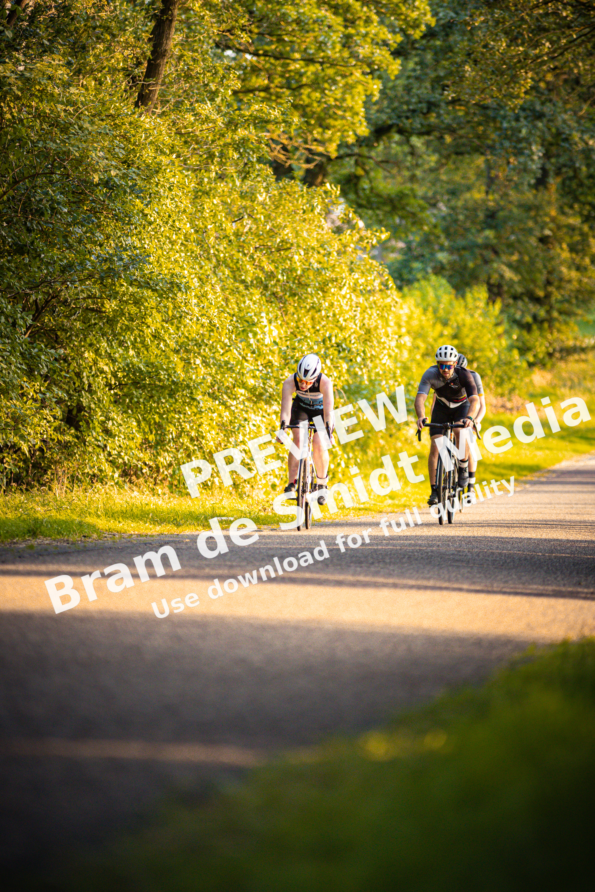 Two cyclists on a paved path, one with a white helmet.