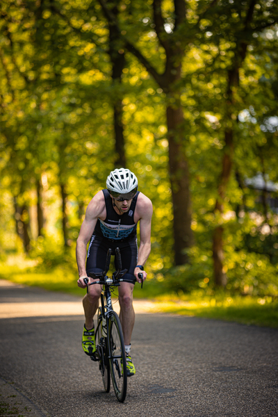 A man is riding a bike on the road while wearing an orange shirt with black and white stripes.