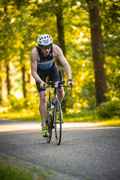 a man riding a bicycle down the road, wearing a triathlon outfit.