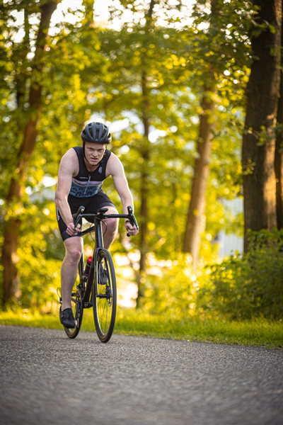 A man in a blue tank top rides a black bicycle down the road.