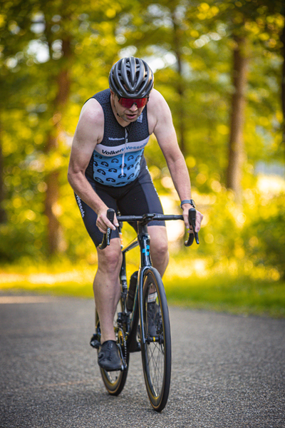 A man in a black and blue tank top rides a bicycle on the road.