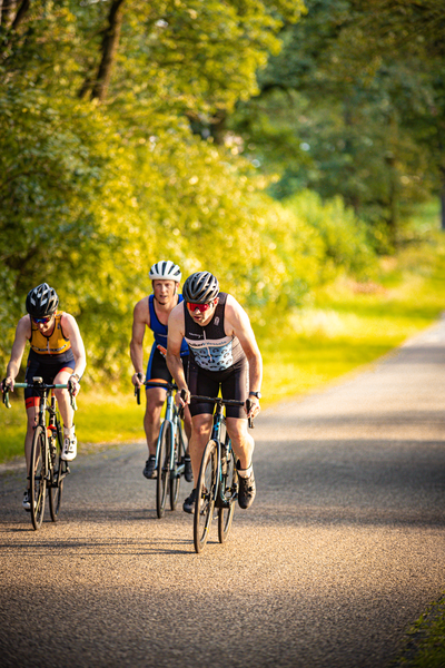 Three cyclists are riding on a gravel path. The person in the middle is wearing a black and white jersey with the number 7.