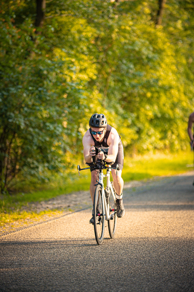 A person riding a bike down the street, in front of green trees and the side of a road.