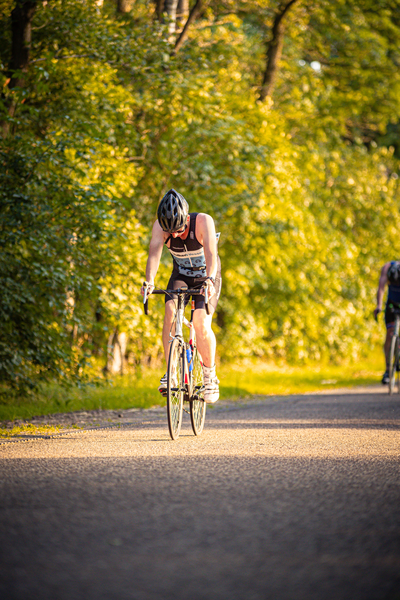 A man in a black helmet is riding a bicycle down a road next to another cyclist.