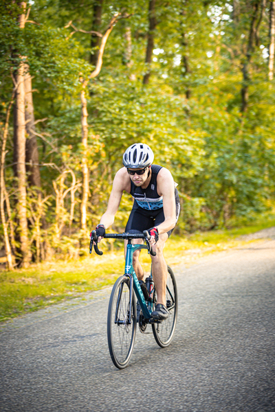 A man riding a bike down the road, he's wearing a black sleeveless shirt and a white helmet.