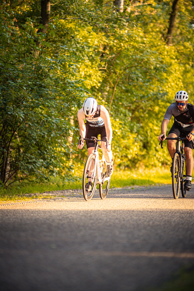 Two cyclists on a road, one in a black and white shirt with the words "triathlon" on it.