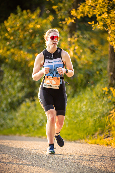 A woman is running on a road wearing an orange race bib with 4199.