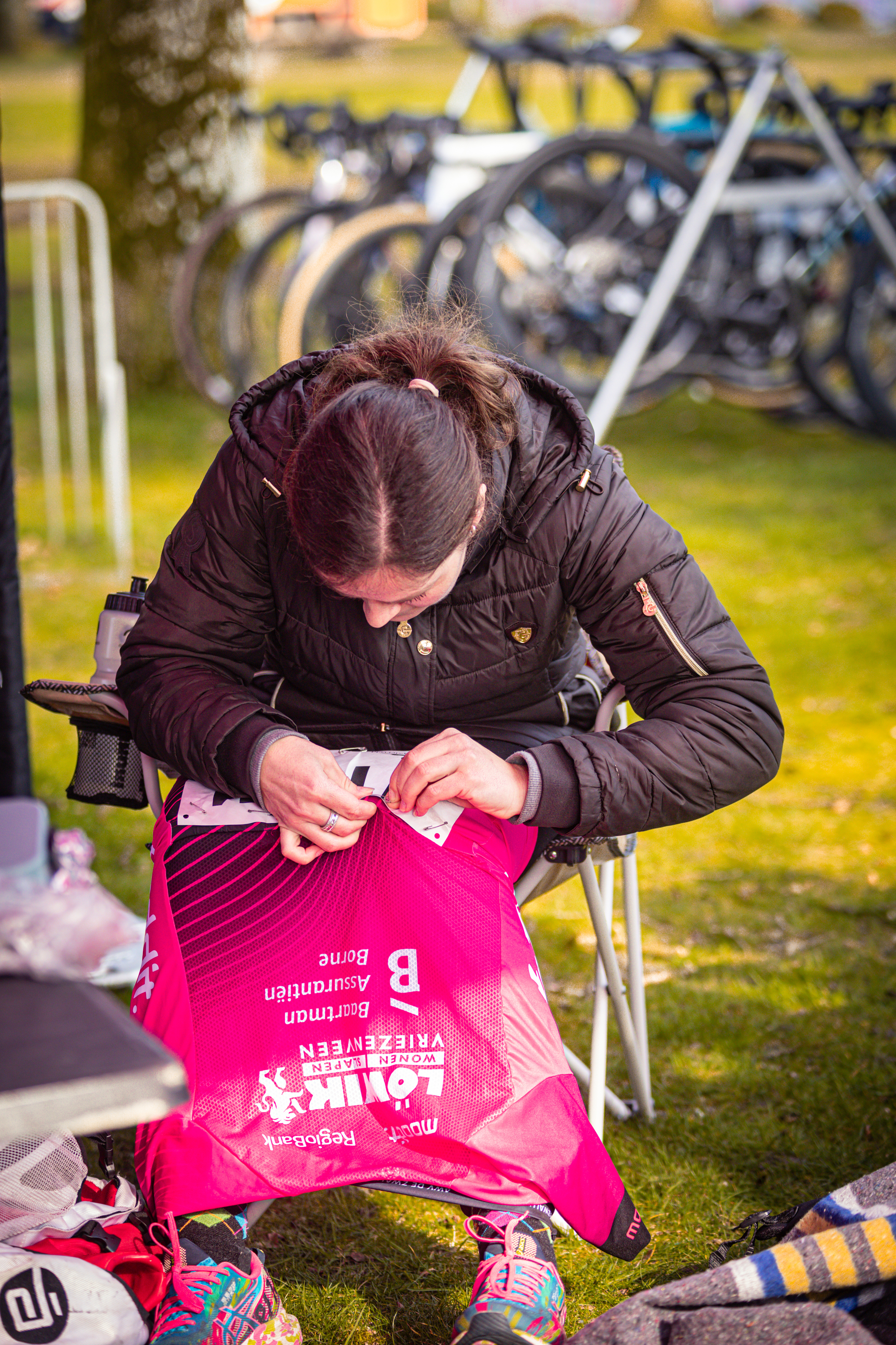 A woman sits cross-legged on the grass, looking at a red bag with yellow text.