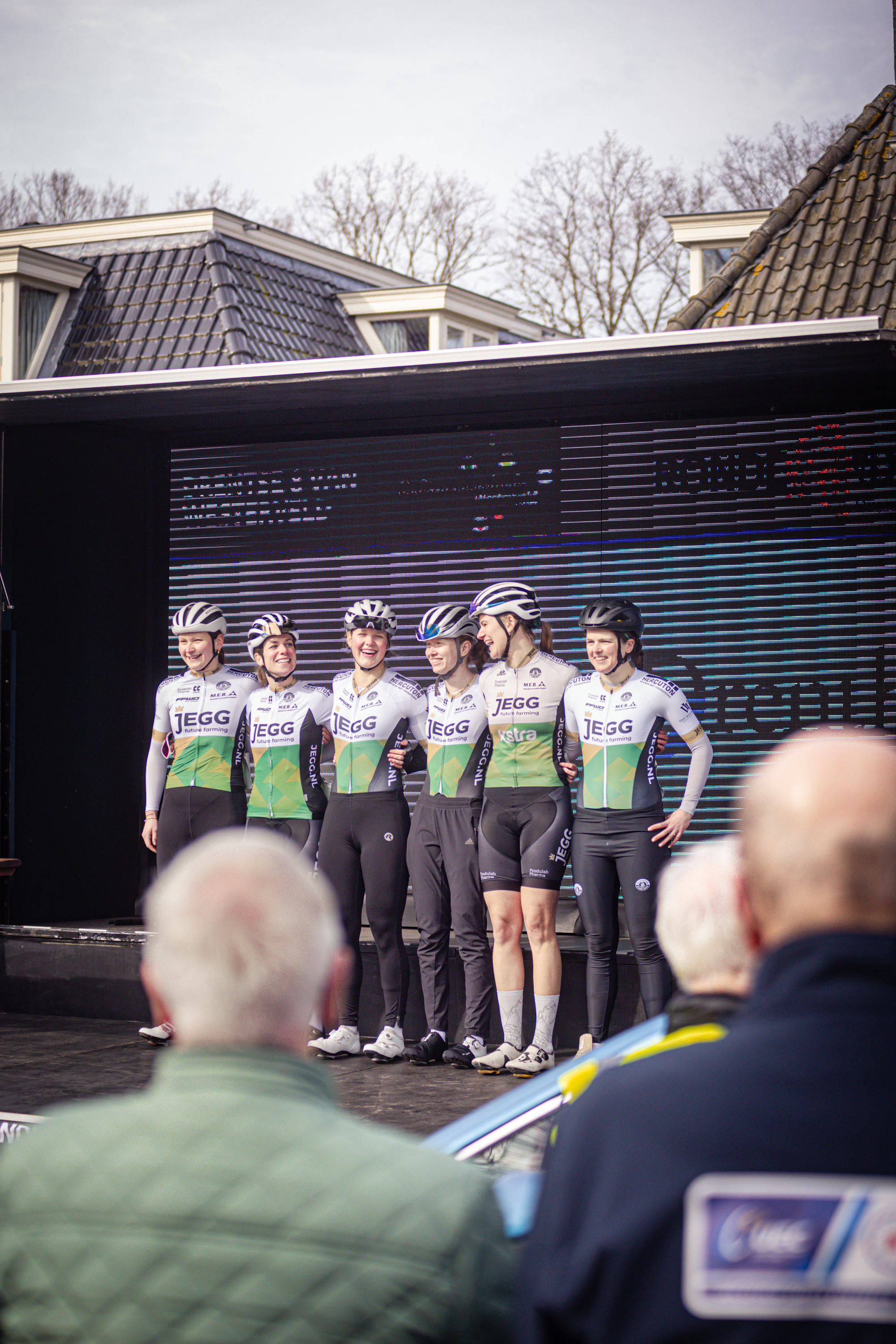 A group of cyclists in matching uniforms are posing on stage for a photo.