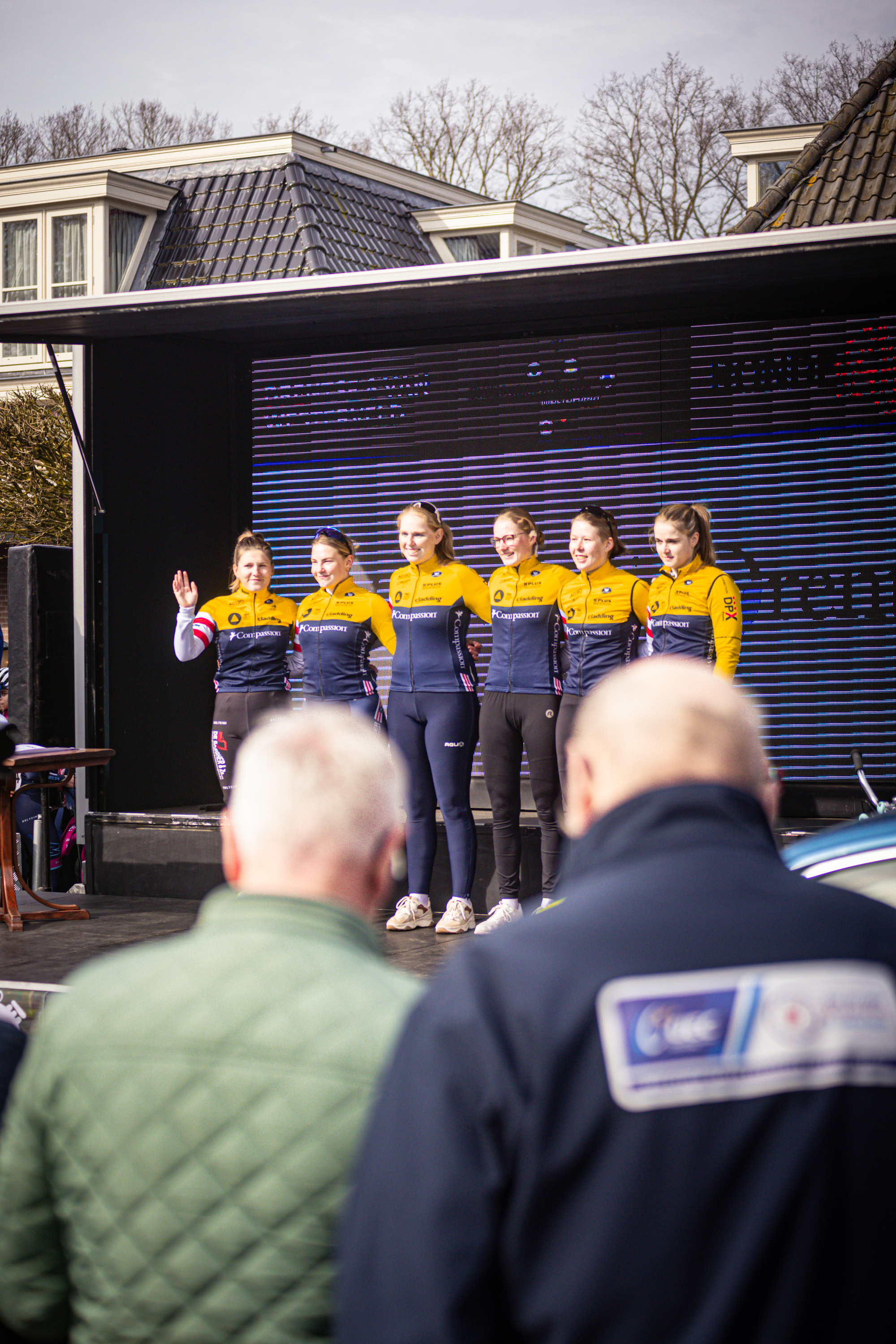 A group of cyclists are lined up for a race on stage in front of a crowd.