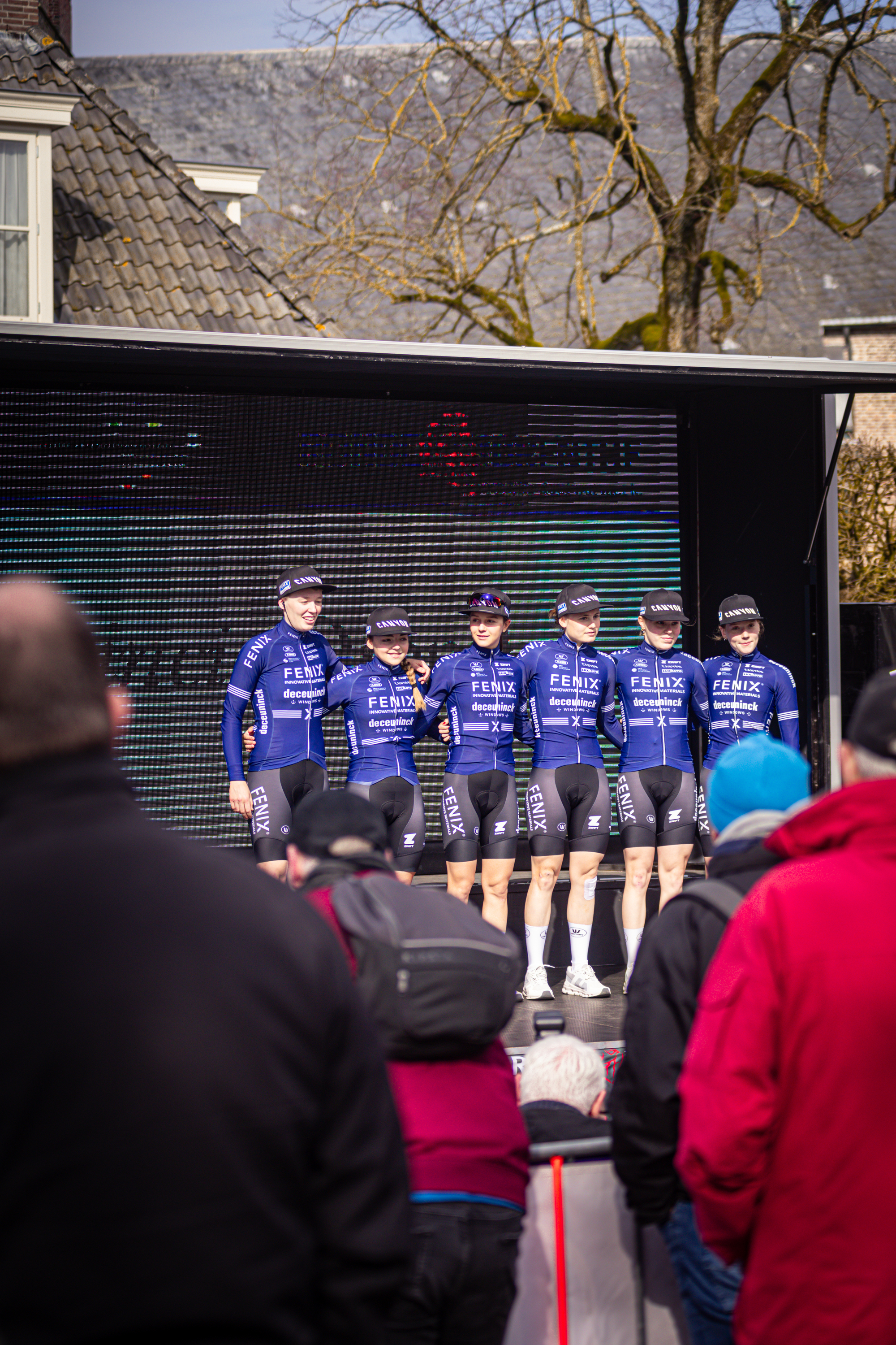 A group of cyclists from Team Wielrennen stand on a stage in front of an audience.