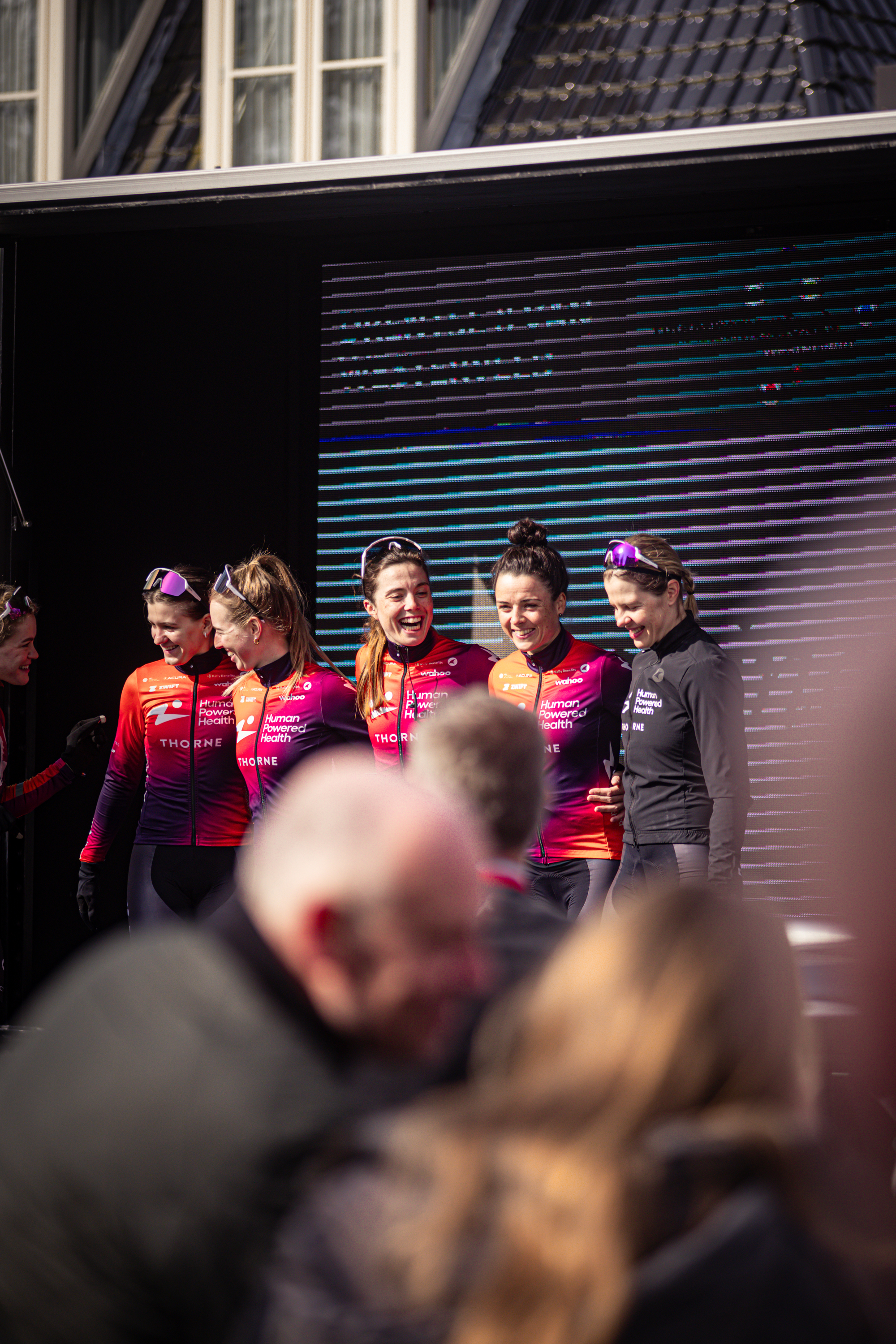 A group of women are wearing matching red cycling outfits and smiling for the camera.