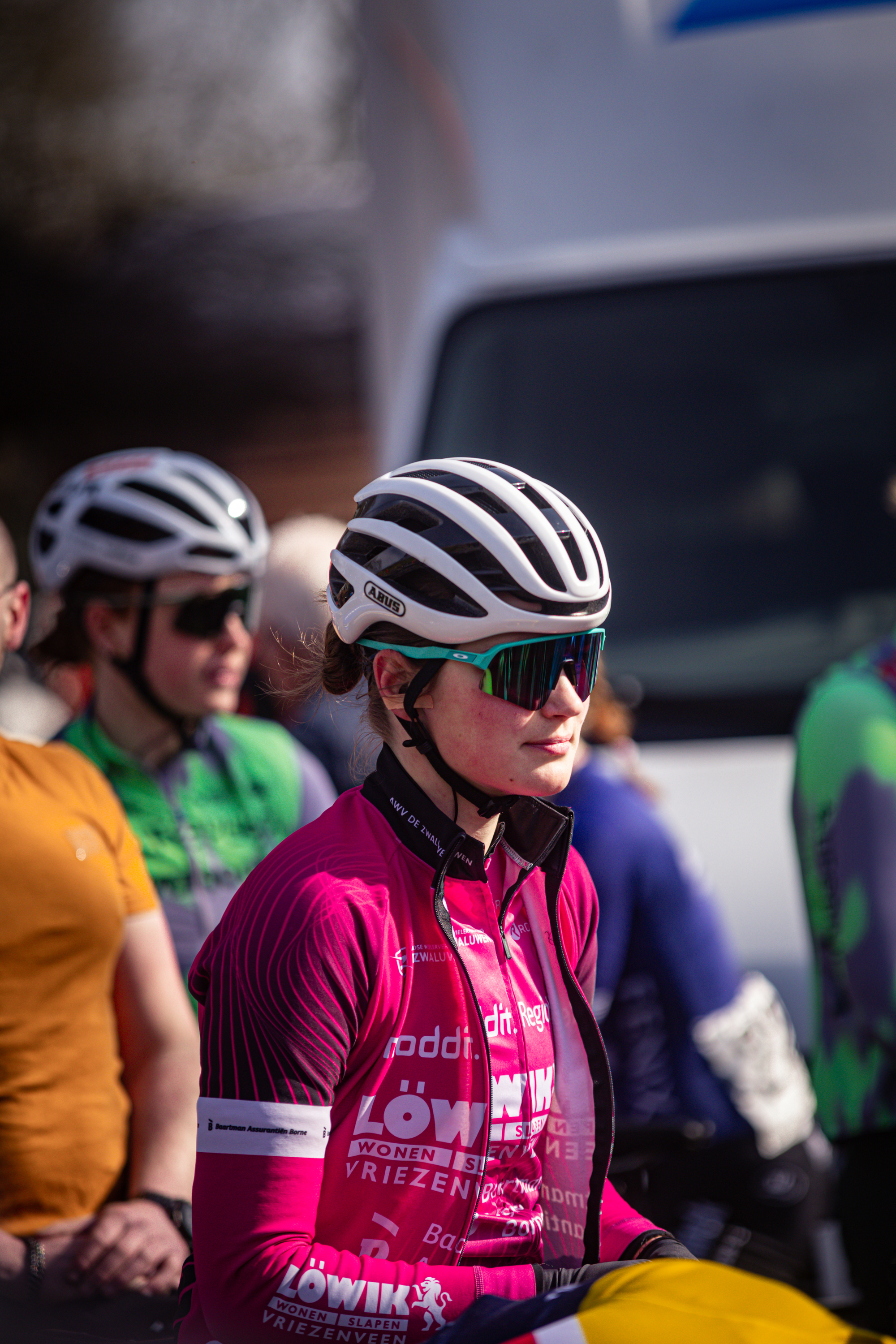 Two cyclists standing in a line wearing safety helmets and pink shirts that say "lowlands".