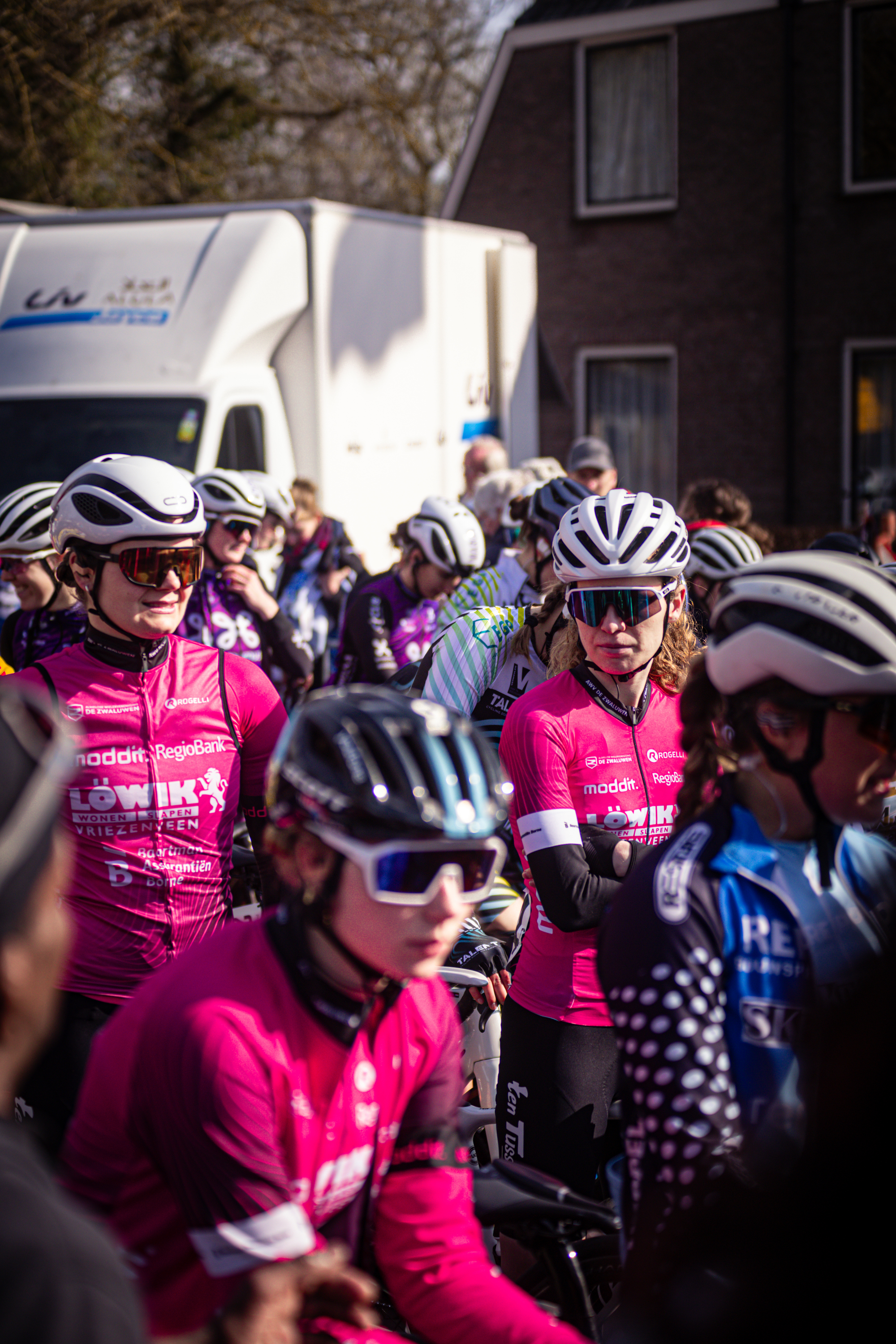 A group of cyclists in bright pink jerseys, getting ready to compete on a sunny day.