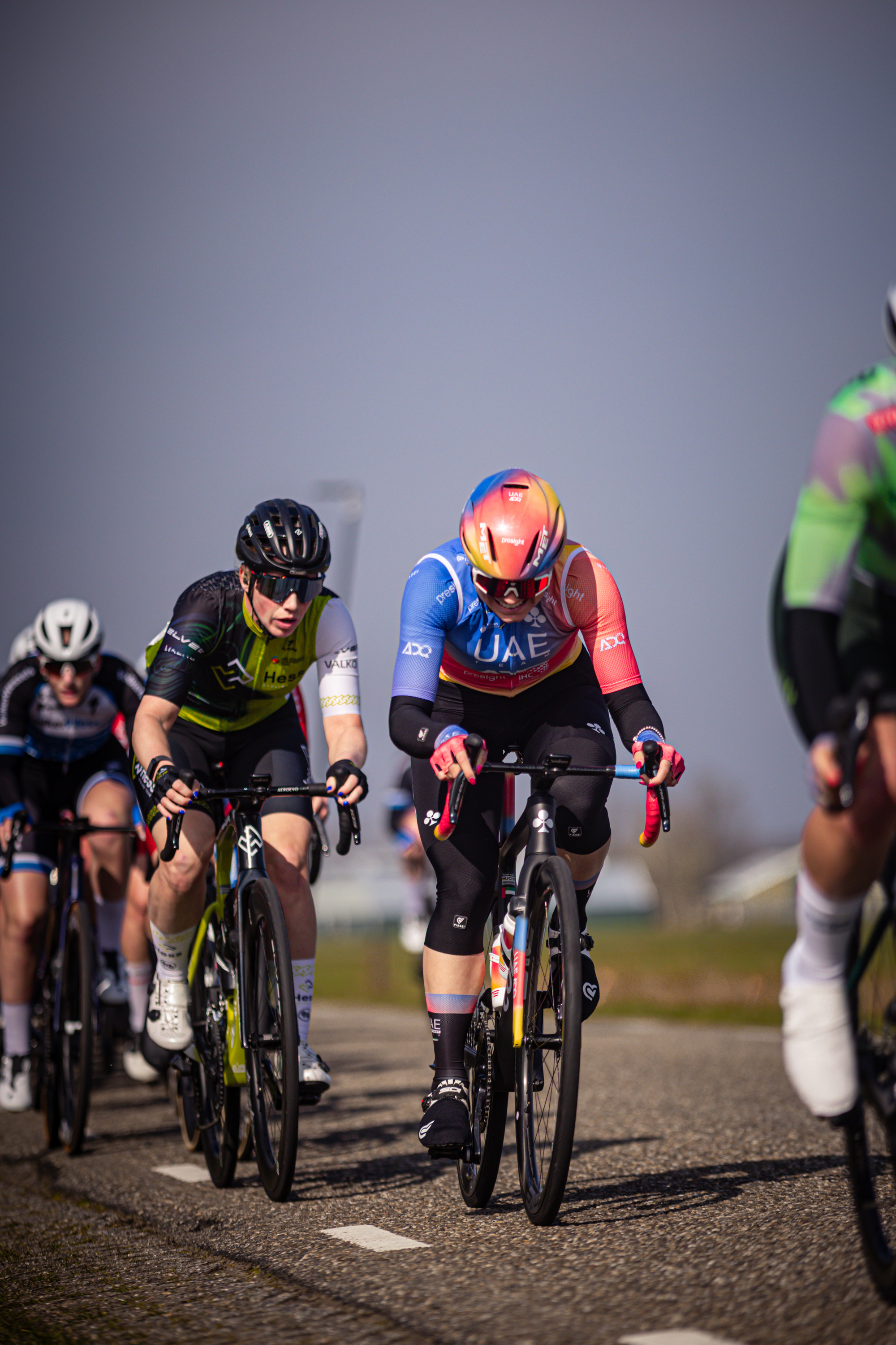 A cyclist in a blue and orange jersey leads a group of cyclists on the road.