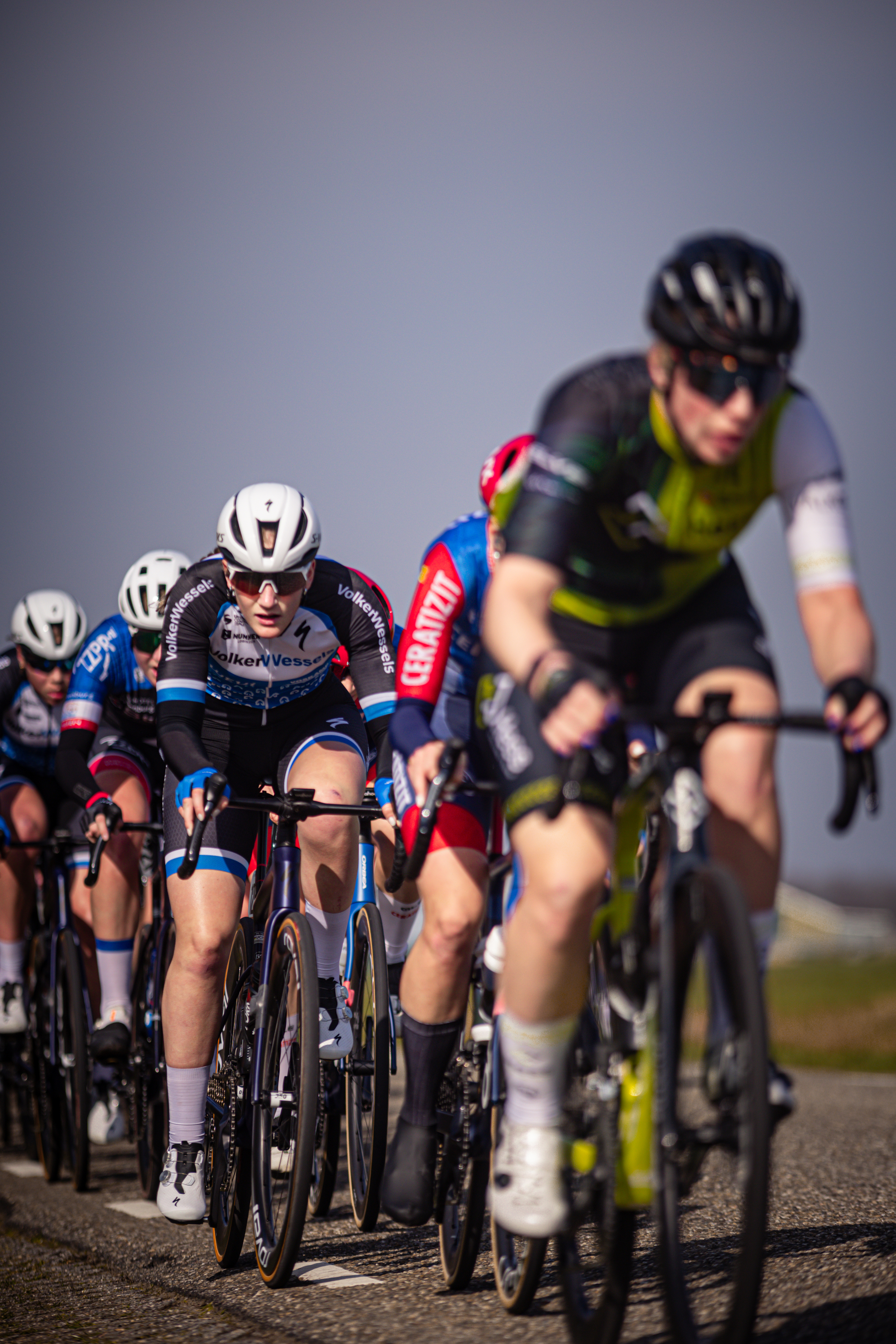 A group of cyclists in a race. The man leading the pack is wearing a green and black shirt and has number 4 on his shirt.