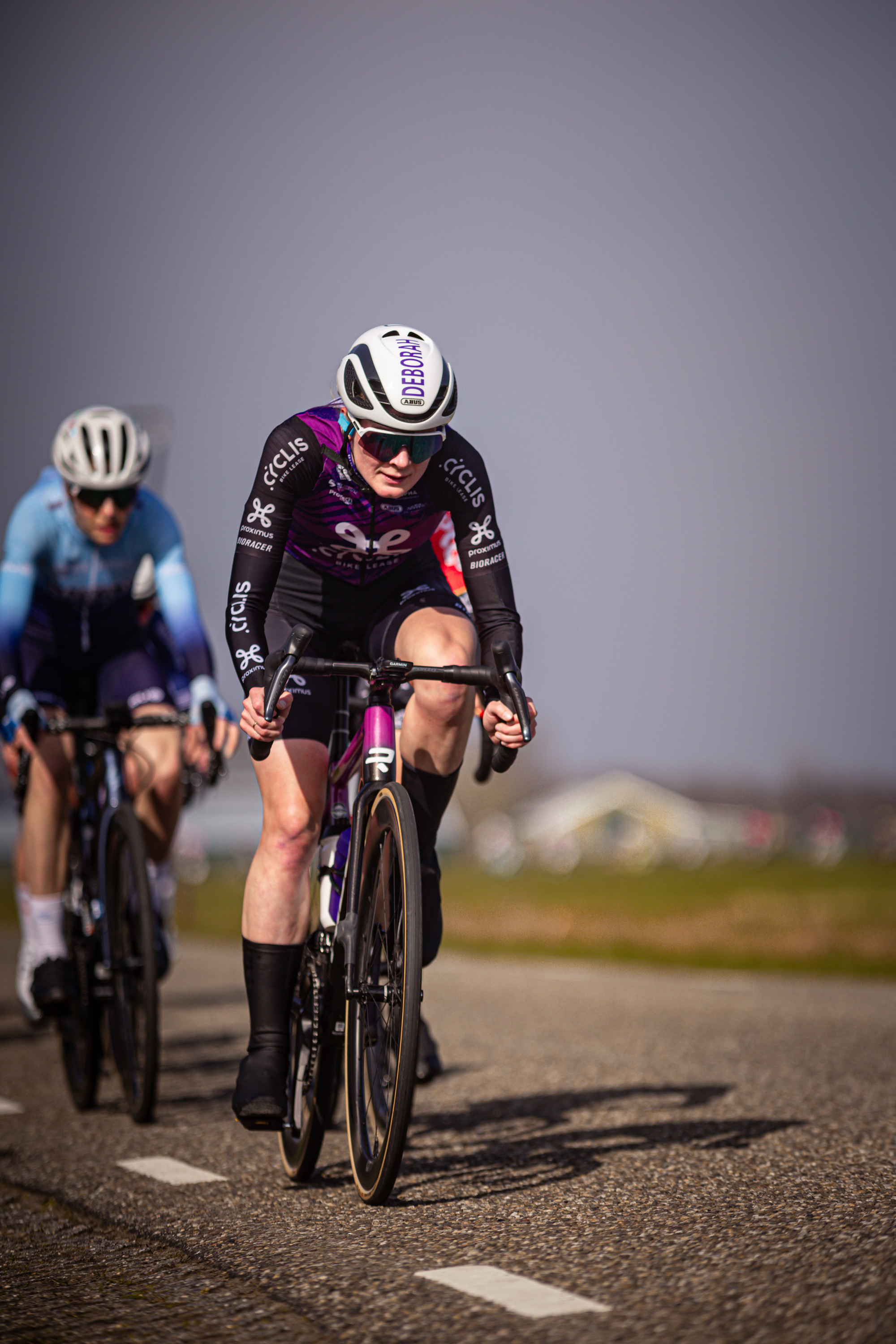 Two cyclists racing on a road with one wearing a purple shirt.