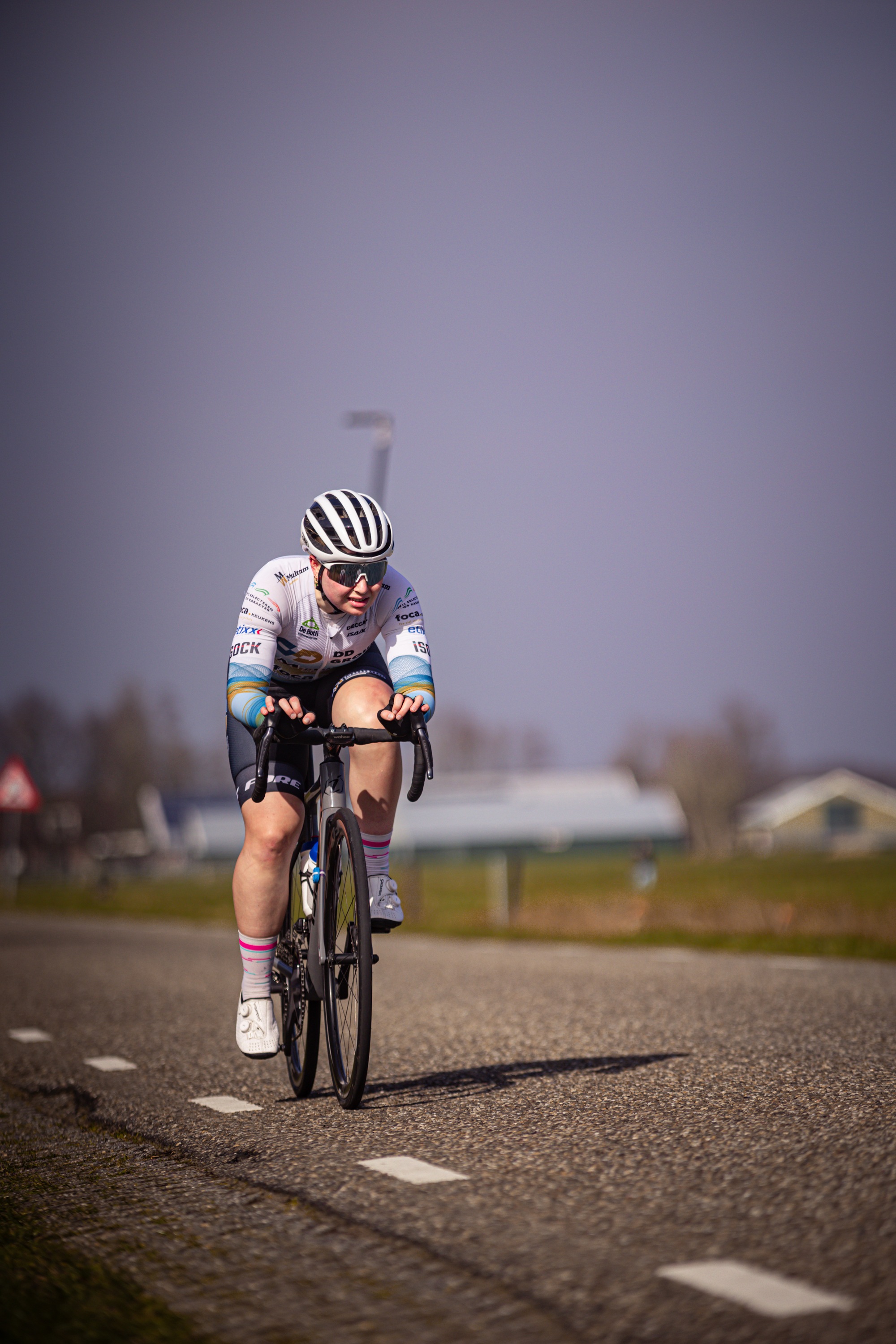 A cyclist in a pink sock and white jersey is riding her bike down the road.