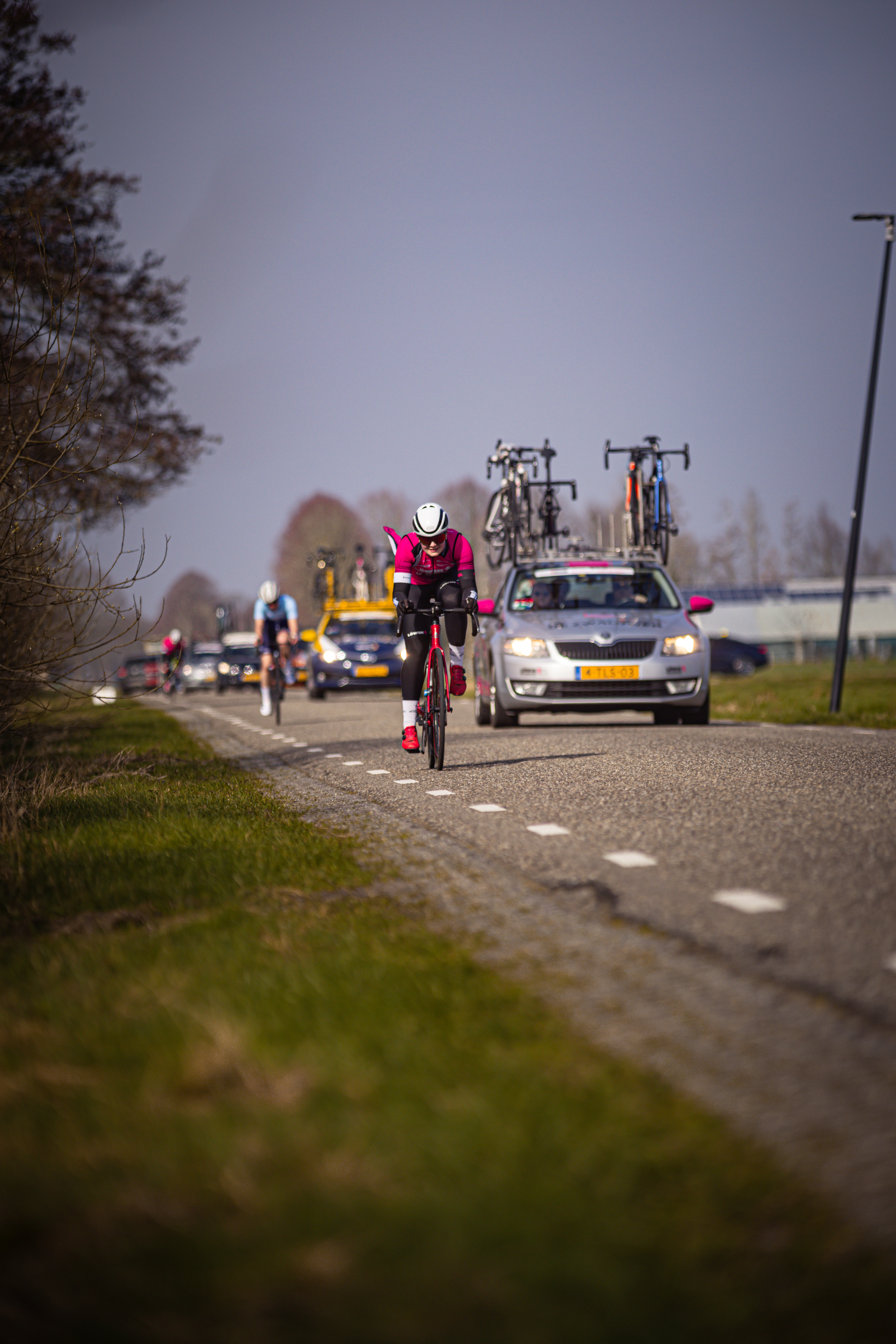 A cyclist on a road with other cyclists and cars behind.