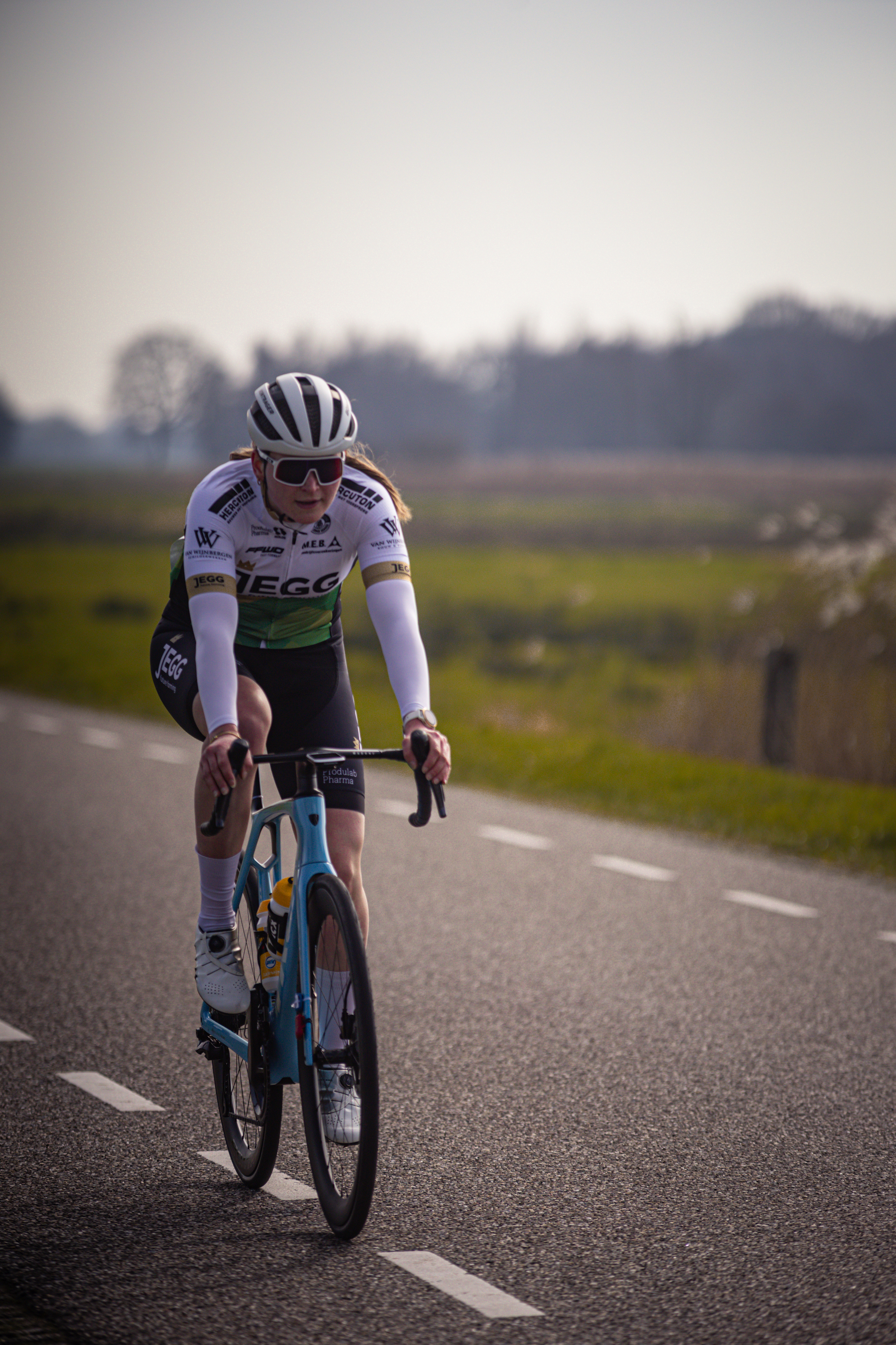 A cyclist wearing a white shirt, black pants and a helmet is riding a blue bike on the road.