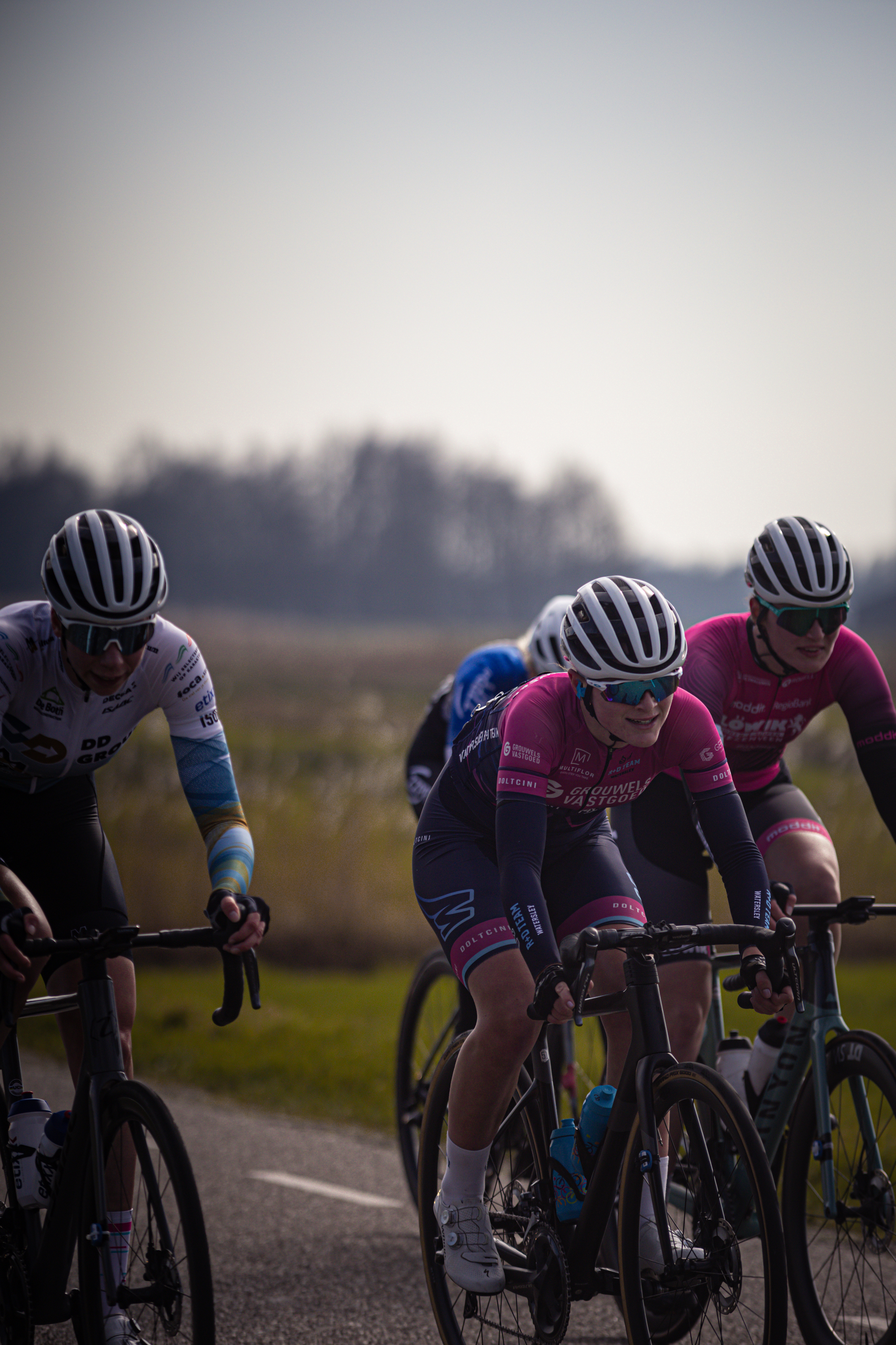 Three cyclists on a road with the number 8 van Westerveld in the background.