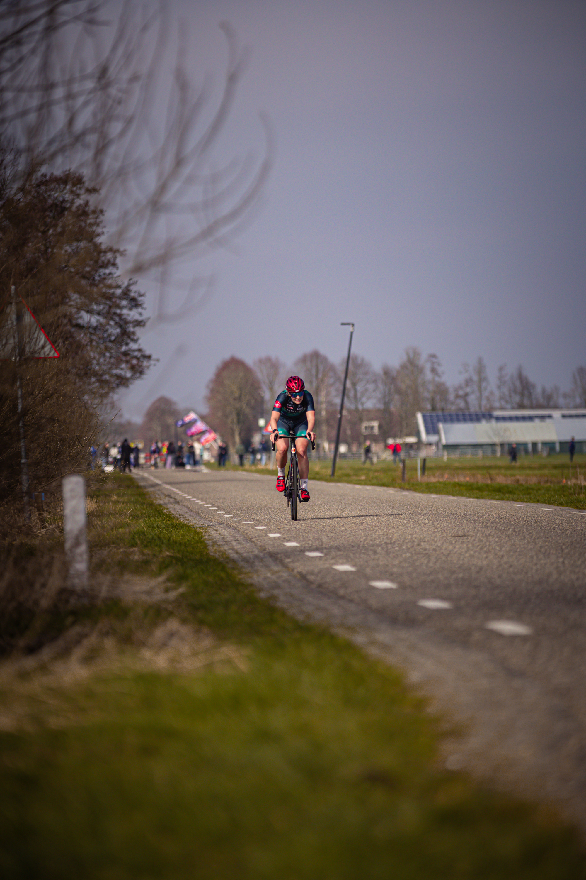 A woman in a red helmet is riding her bike down the road as seen from the side of the street.