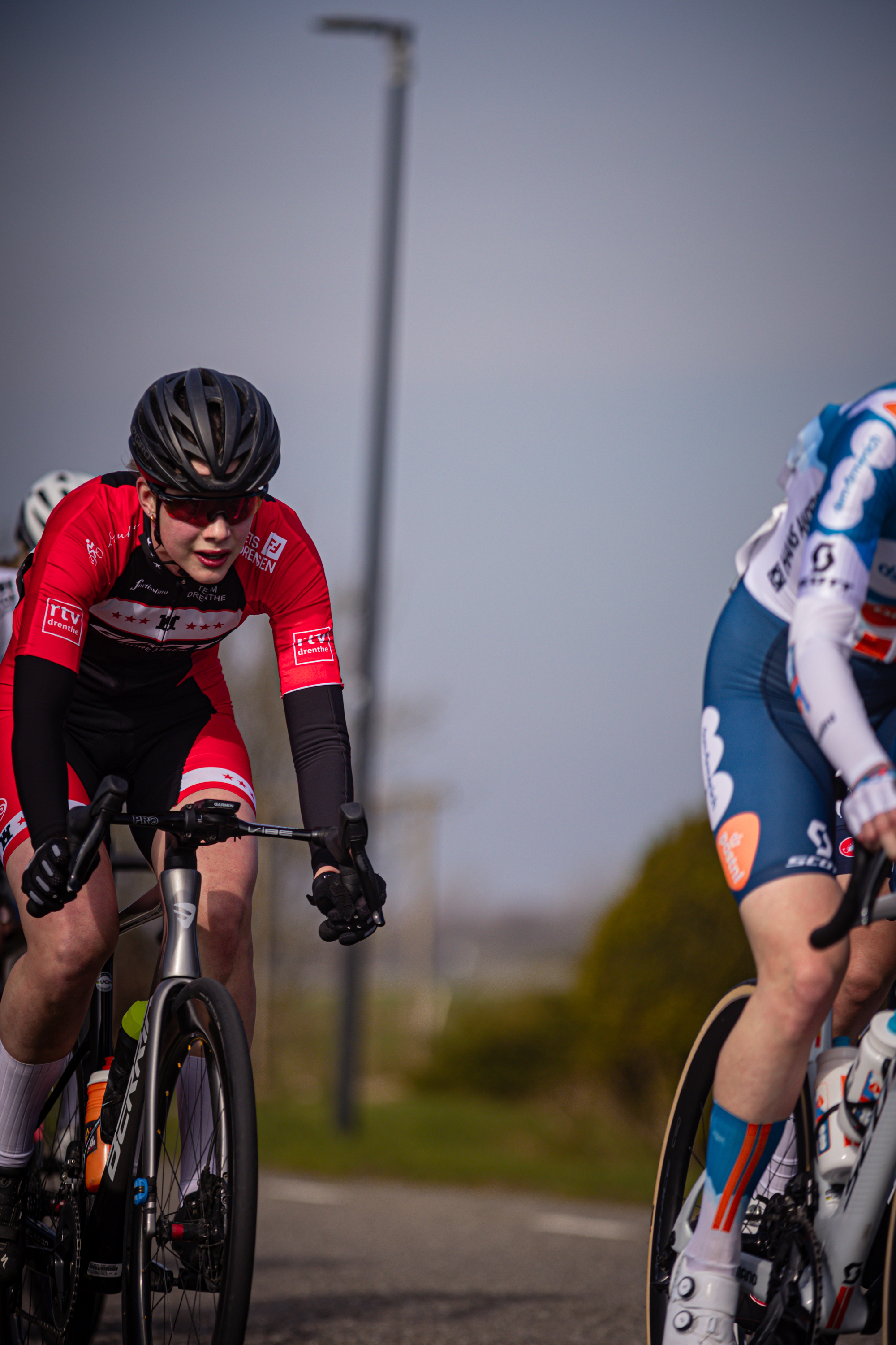 Two cyclists racing on a track with one wearing an orange and black jersey with the letter A on it.