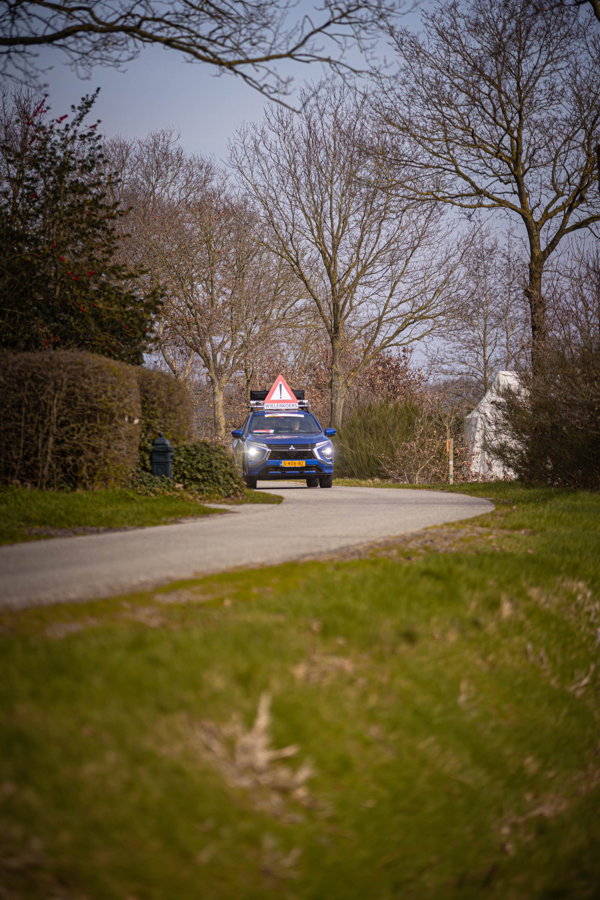 A blue race car drives down the street of Wielrennen, Drentse 8 van Westerveld.