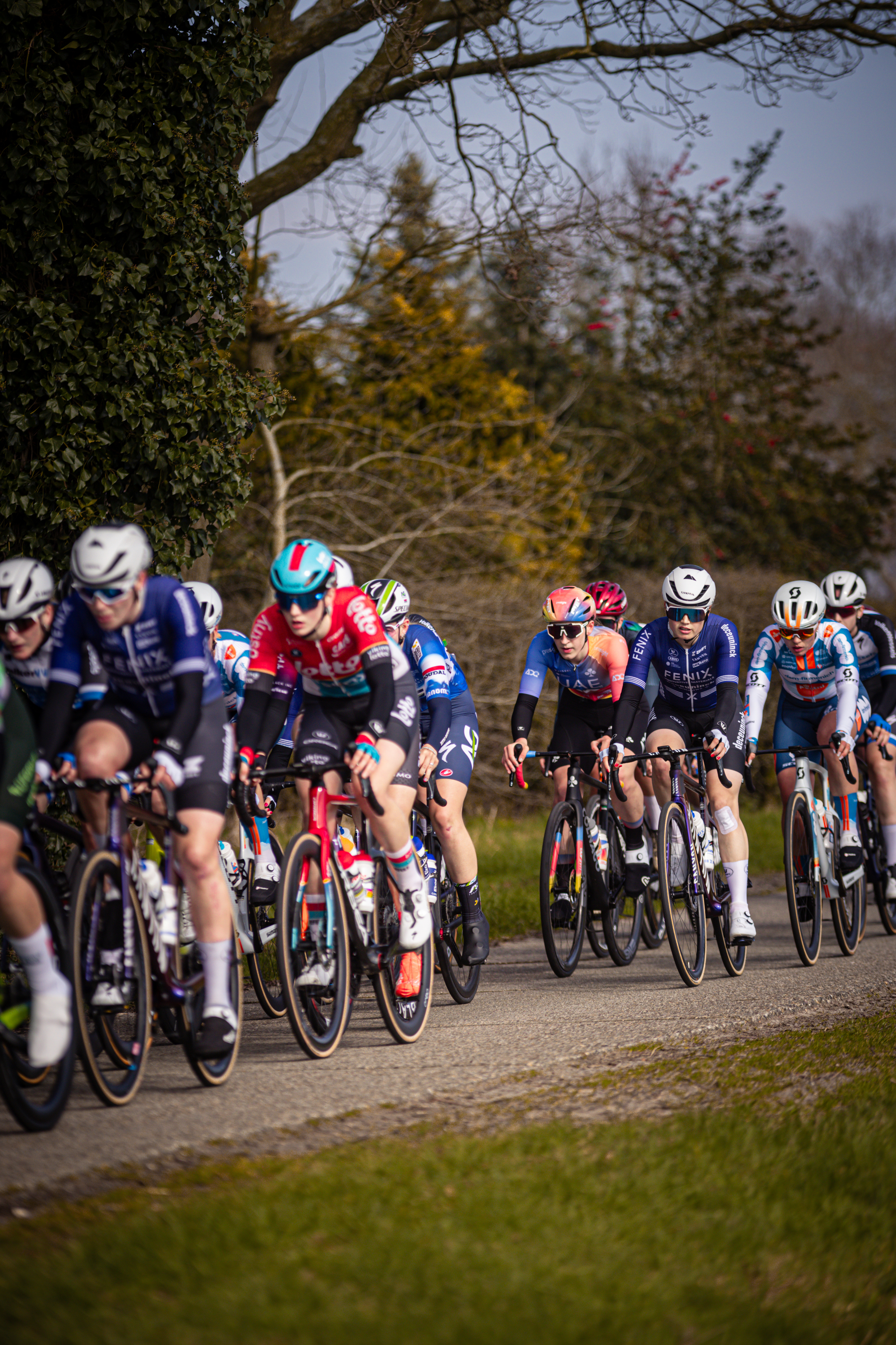 Several cyclists wearing blue and red outfits are riding on a gravel road.