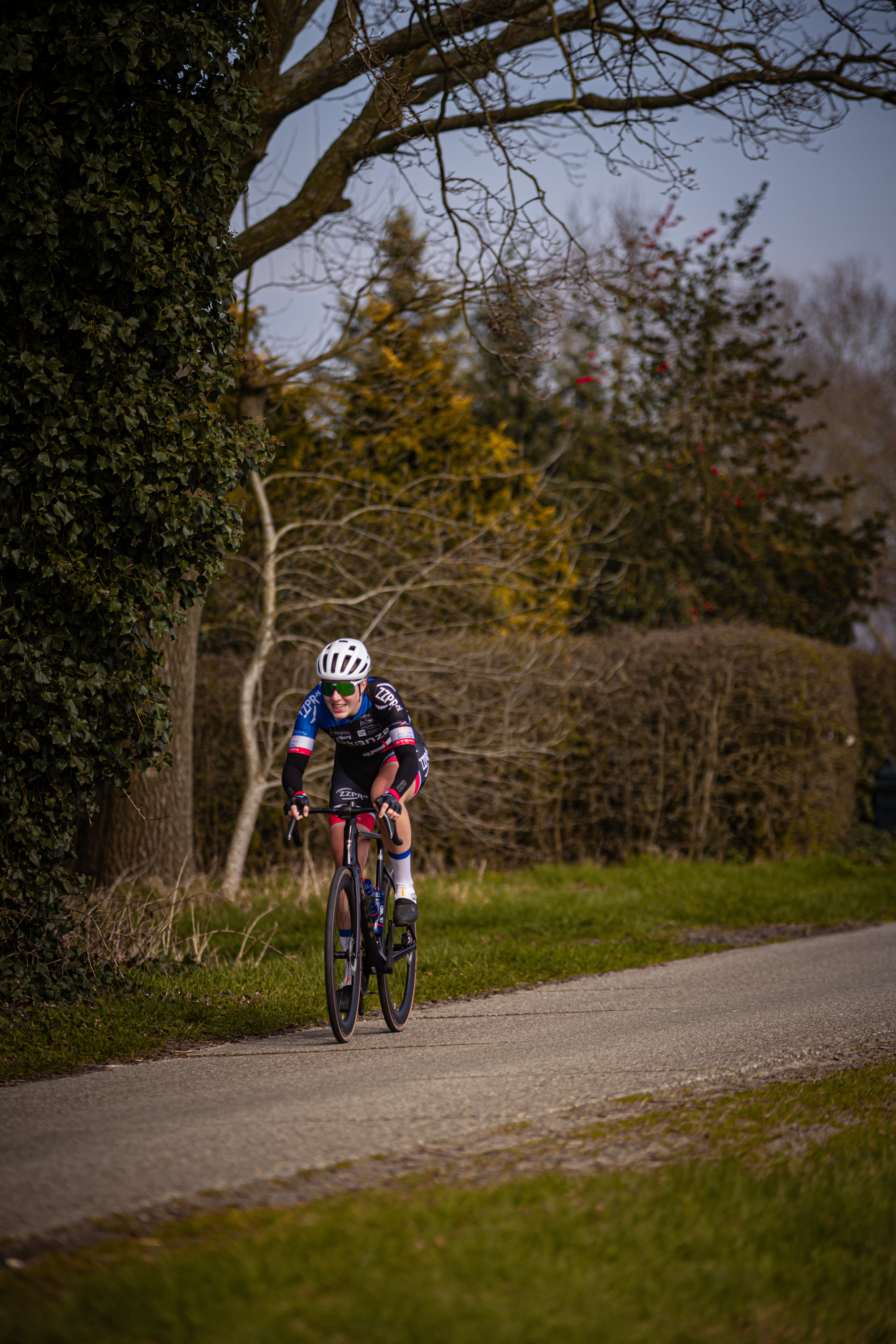 A man in a blue and black jersey is riding a bike along the side of a road.