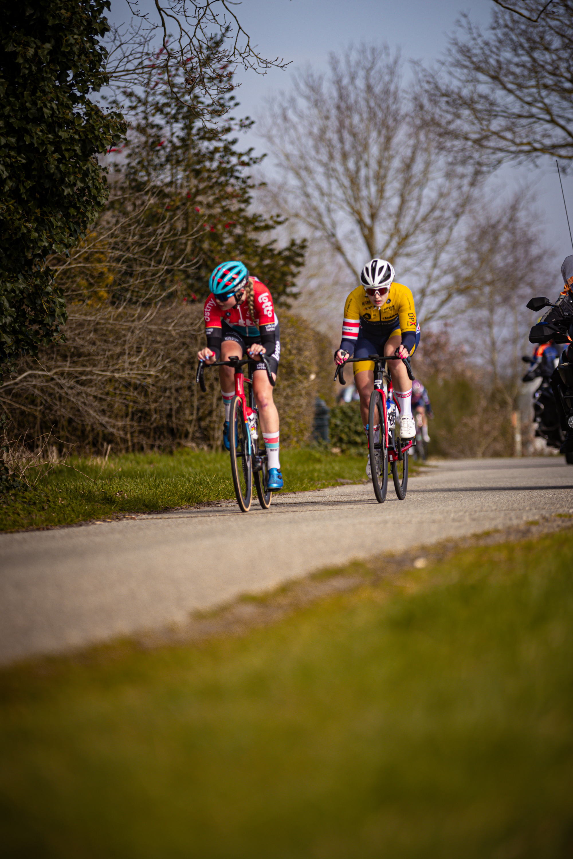 Two cyclists are seen riding down a road on the Wielrennen.