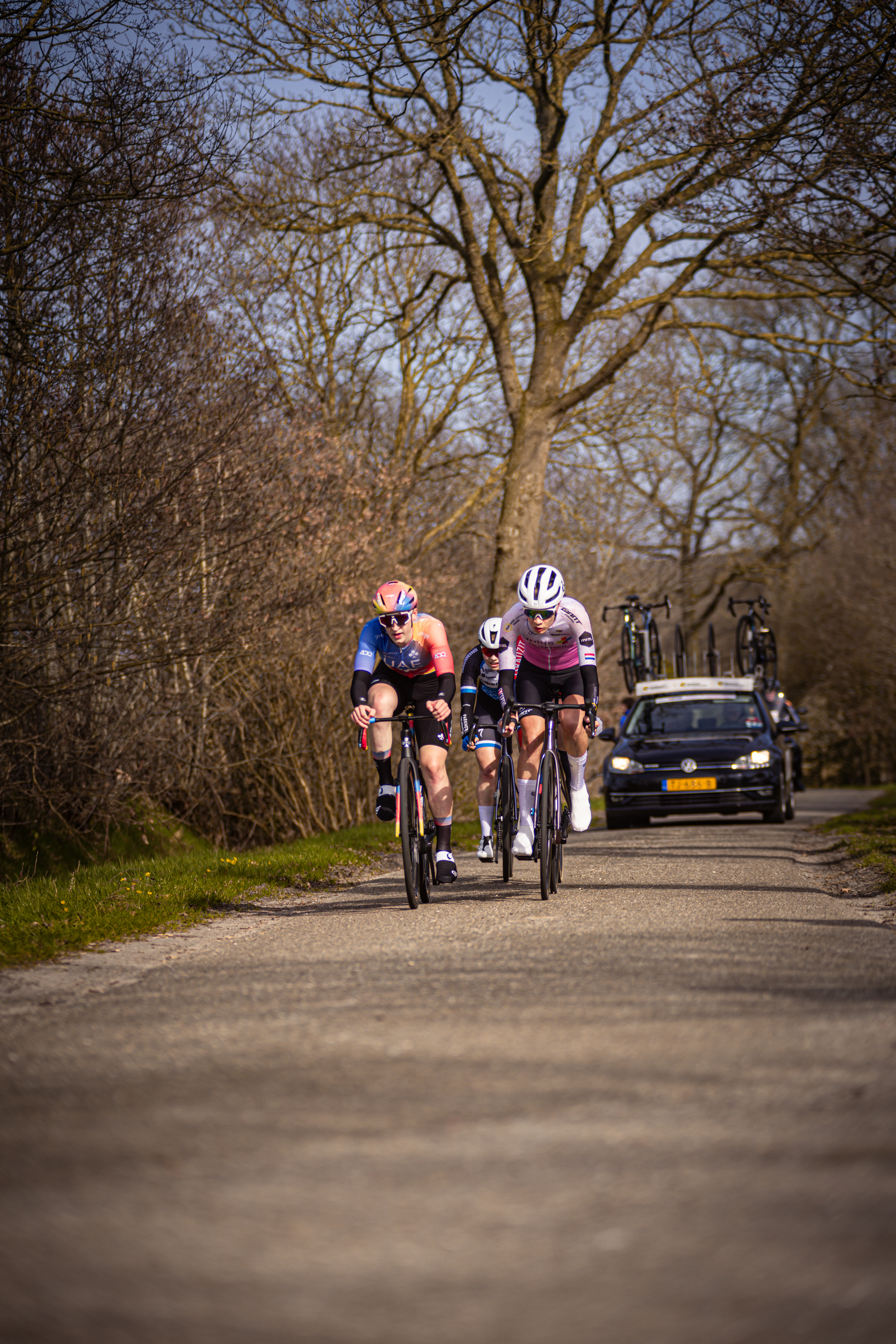 Three cyclists are riding on a dirt road in the countryside.