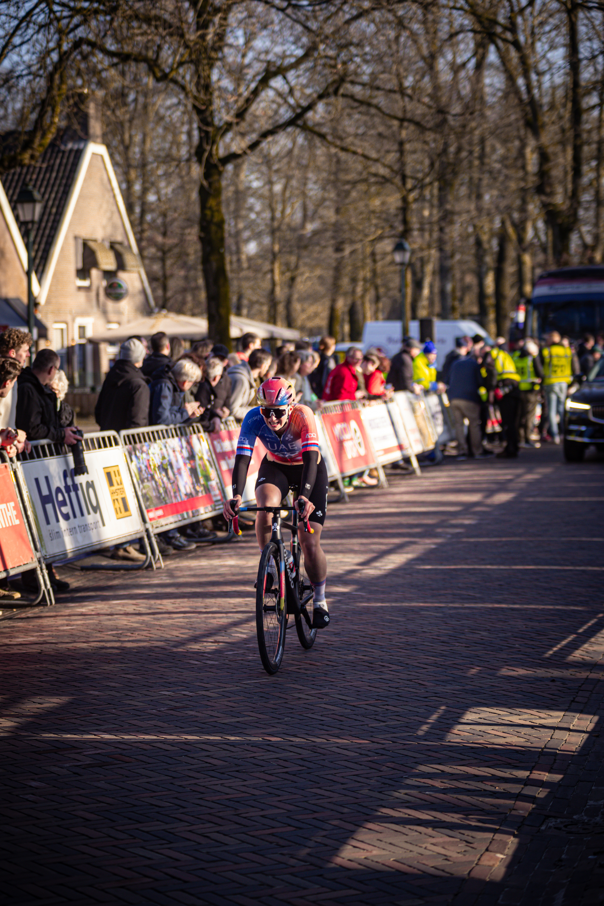 A person riding a bicycle on a cobblestone road with a group of people watching.