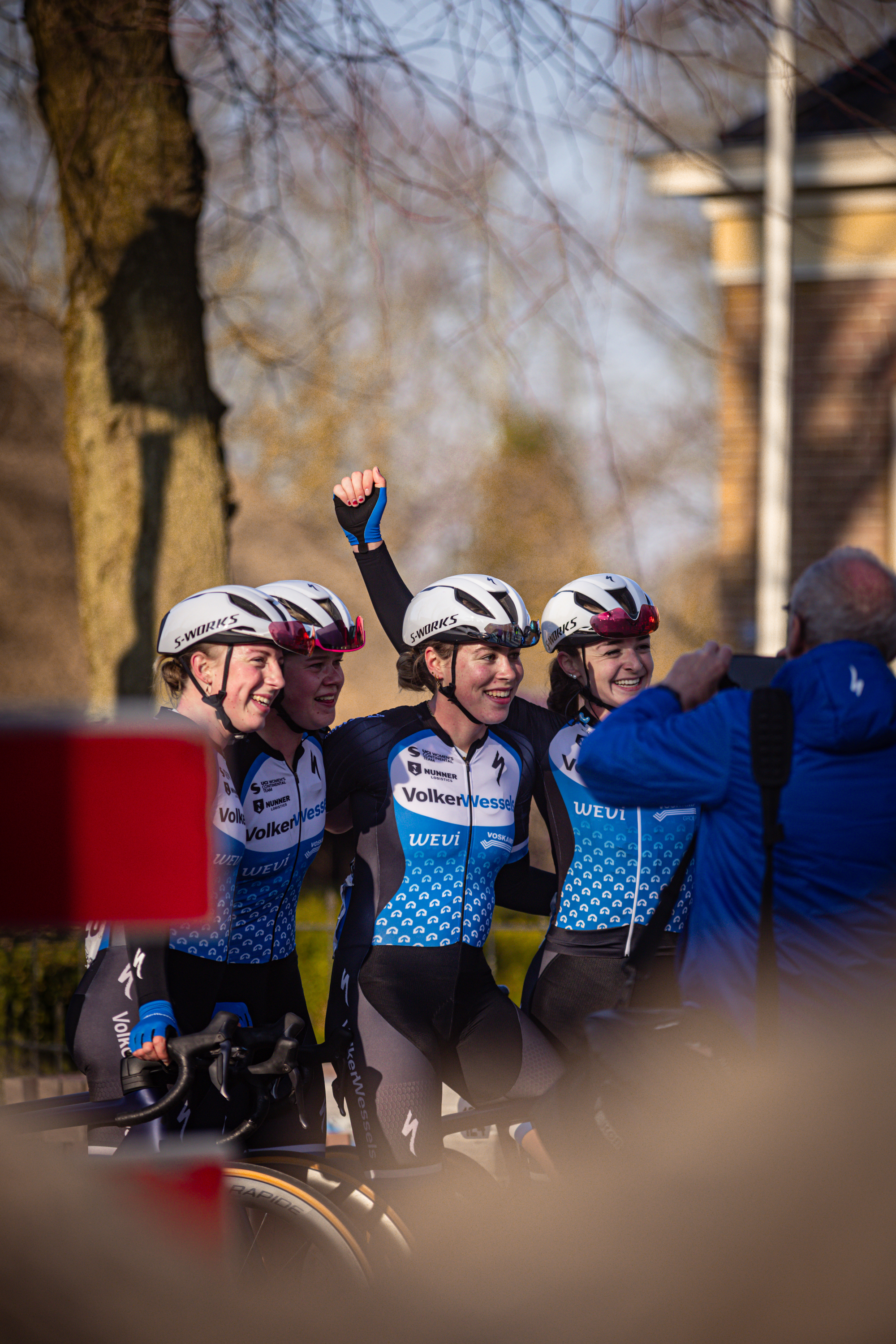 Wielrennen is an event in 2024 where participants are wearing blue and white outfits. They have their arms up, celebrating.