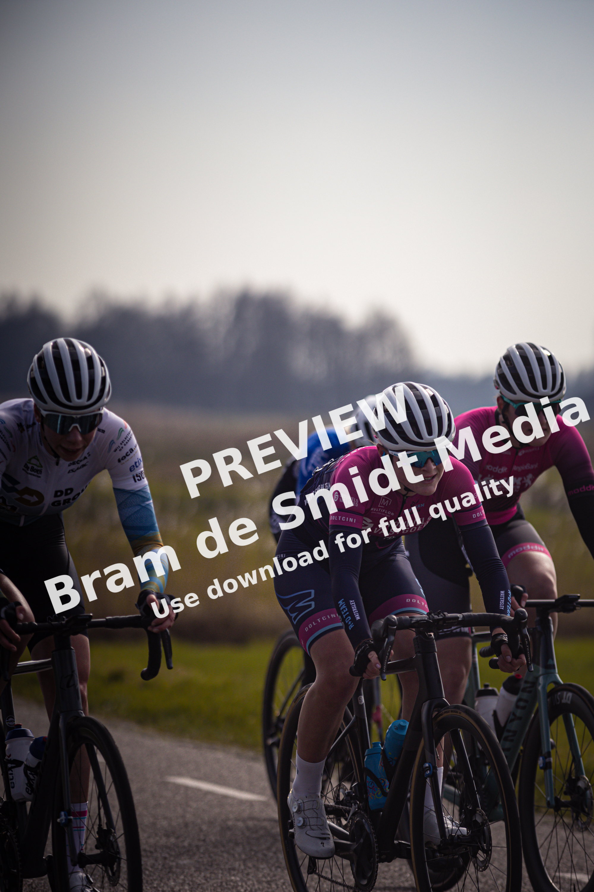 Three cyclists on a road with the number 8 van Westerveld in the background.