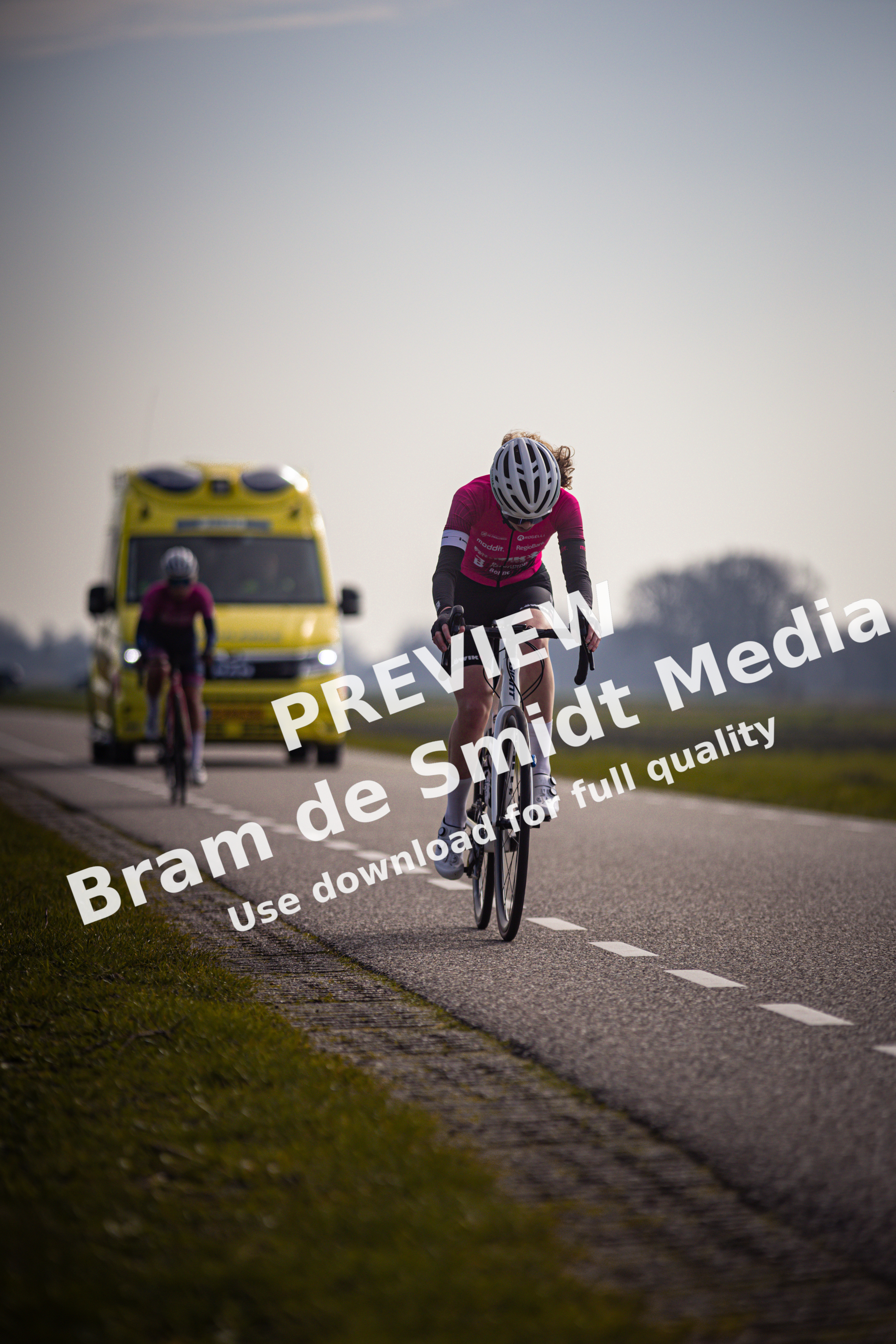 A woman riding a bicycle past another cyclist and a yellow bus.