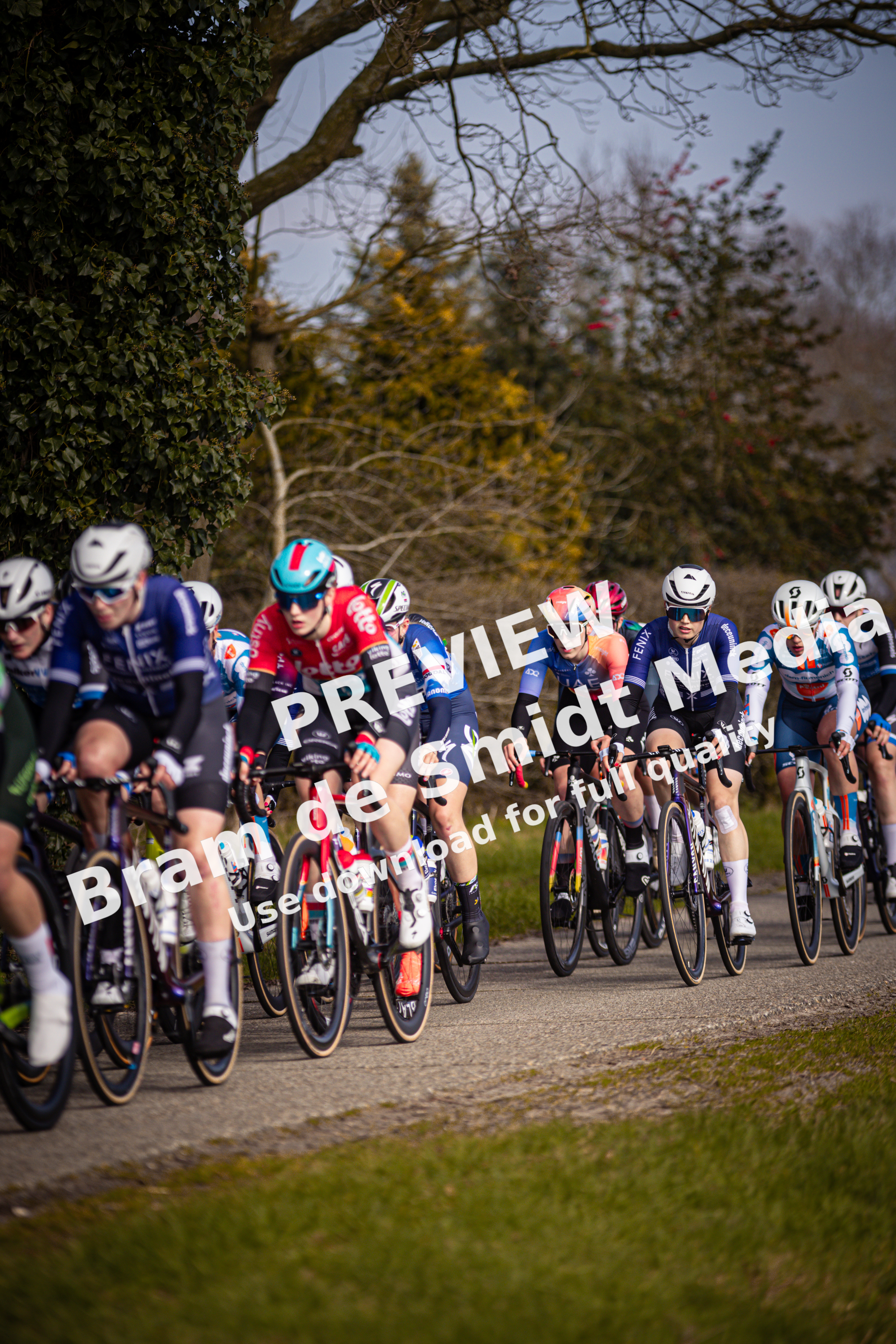 Several cyclists wearing blue and red outfits are riding on a gravel road.