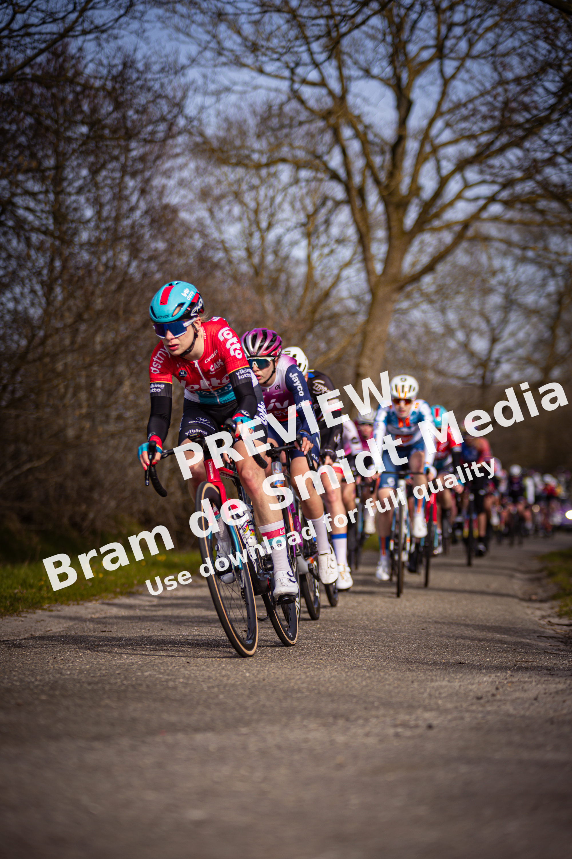A man and woman race their bikes on a road. The man is wearing a red jersey with the number 27 on it.