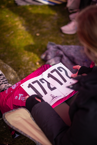 A woman sits on the grass, holding a race bib with the number 172122.