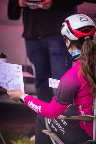 A person wearing a helmet and a pink jersey is holding a paper map while sitting on a chair.