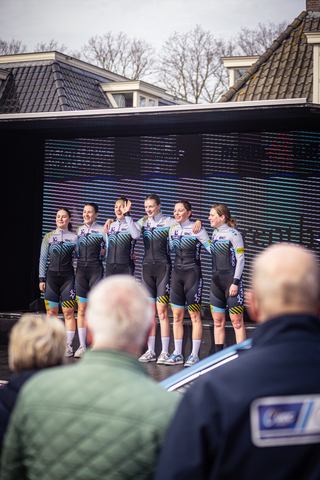 A group of 5 female cyclists standing in a line on a stage.