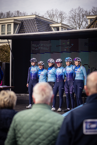 Five cyclists standing in a line up with one another.