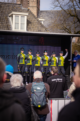 A group of cyclists standing in front of a large banner for the Tour De France.