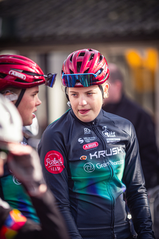 Two female cyclists are at a race event on a sunny day.