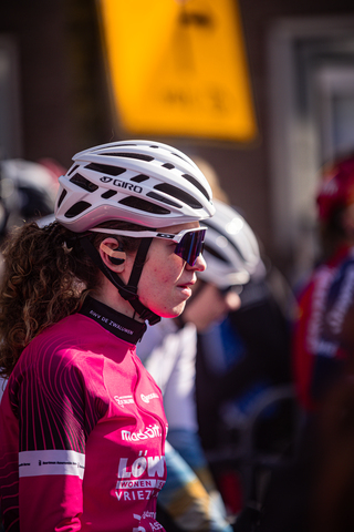 A young woman in a red Wielrennen cycling uniform is wearing a black helmet and glasses.