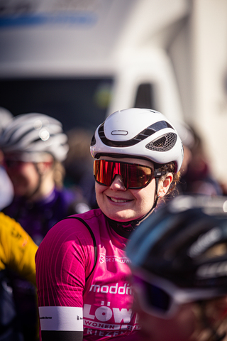 A woman wearing a white and black helmet is standing outside on a sunny day.