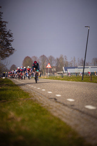 A group of cyclists participate in a race near a sign that warns of traffic.