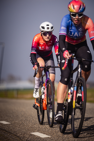 Two cyclists are on a road, with the one in the orange jersey wearing number 14. They are riding together.